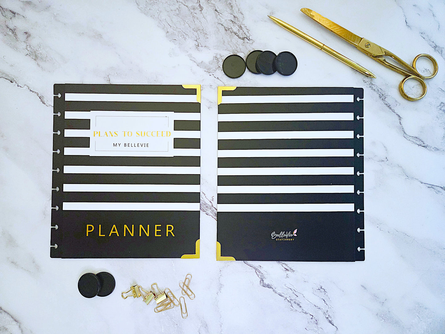 Black and gold planner with accessories on a marble surface