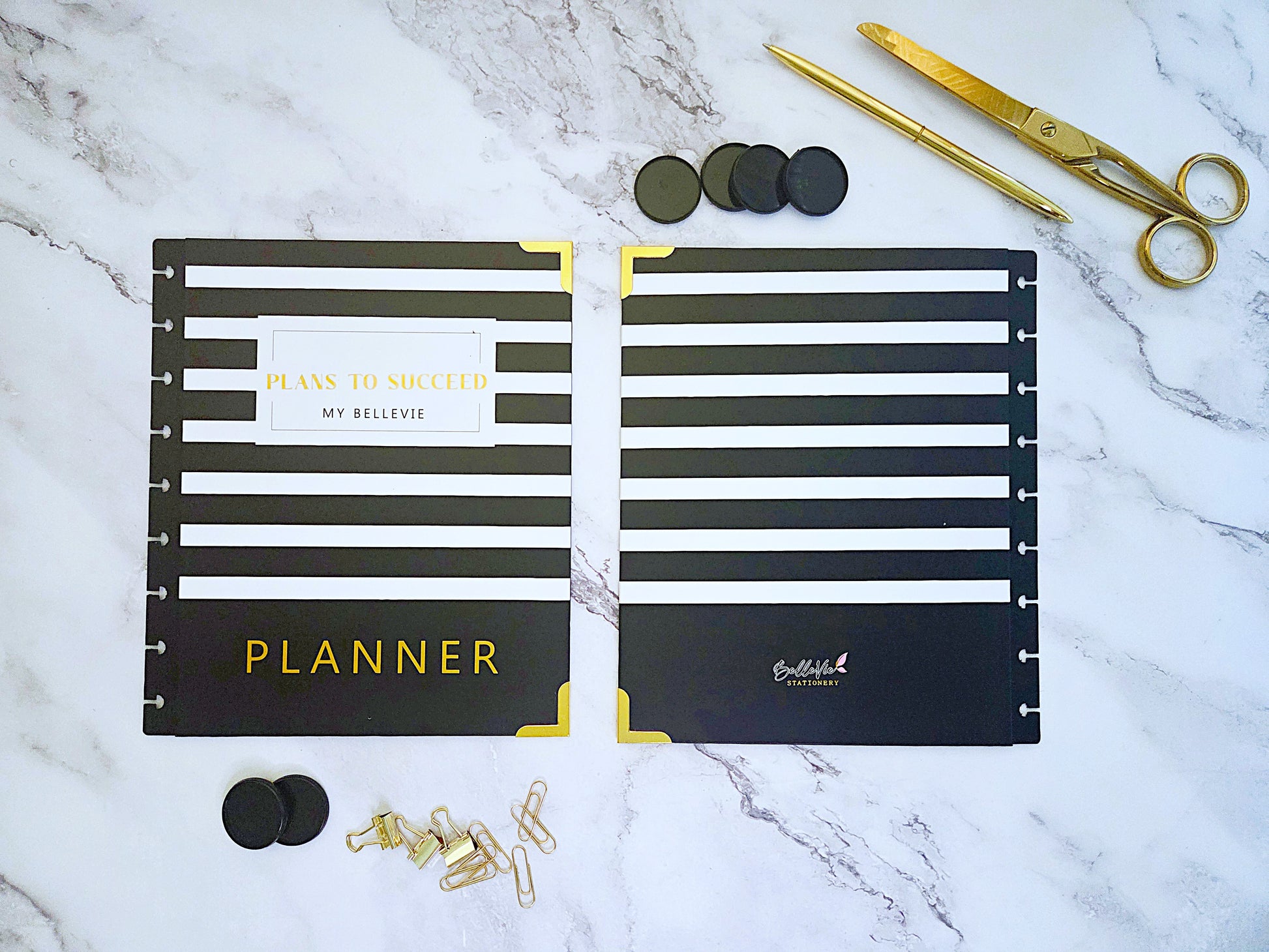Black and gold planner with accessories on a marble surface