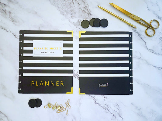 Black and gold planner with accessories on a marble surface